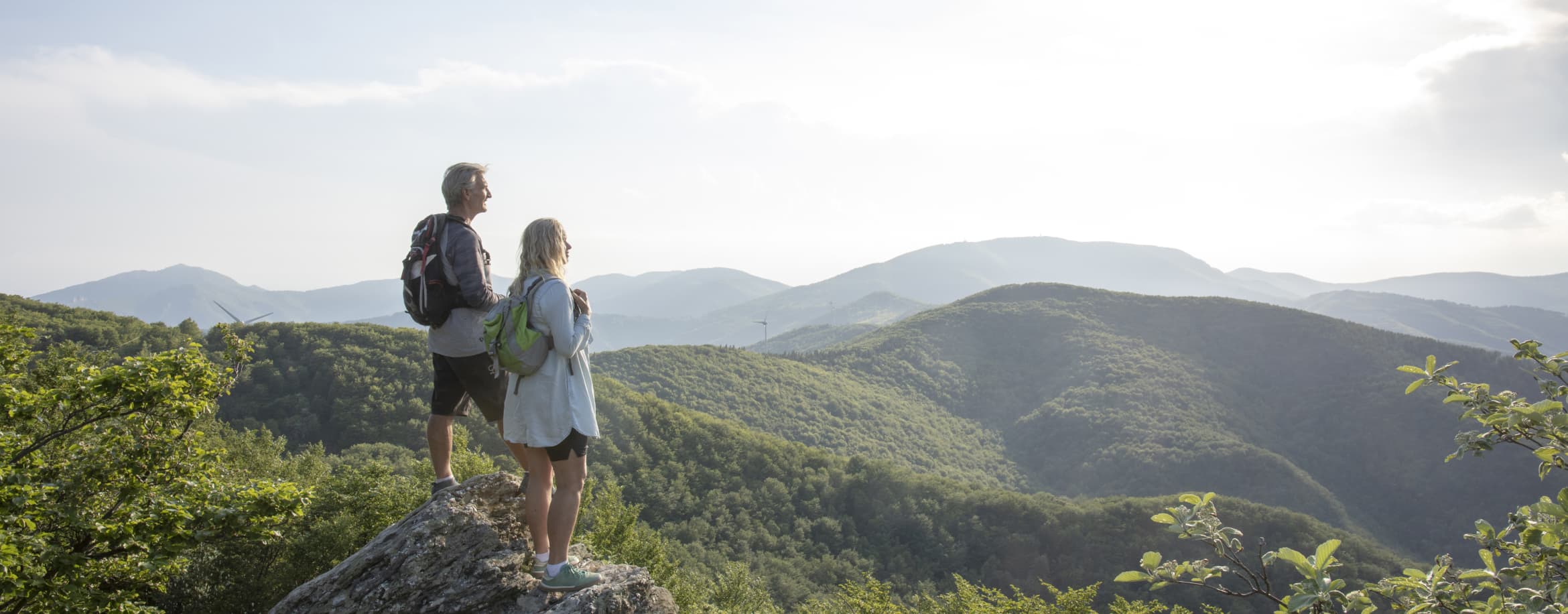 A retired couple standing together on a grassy hillside, looking out over the valley below
